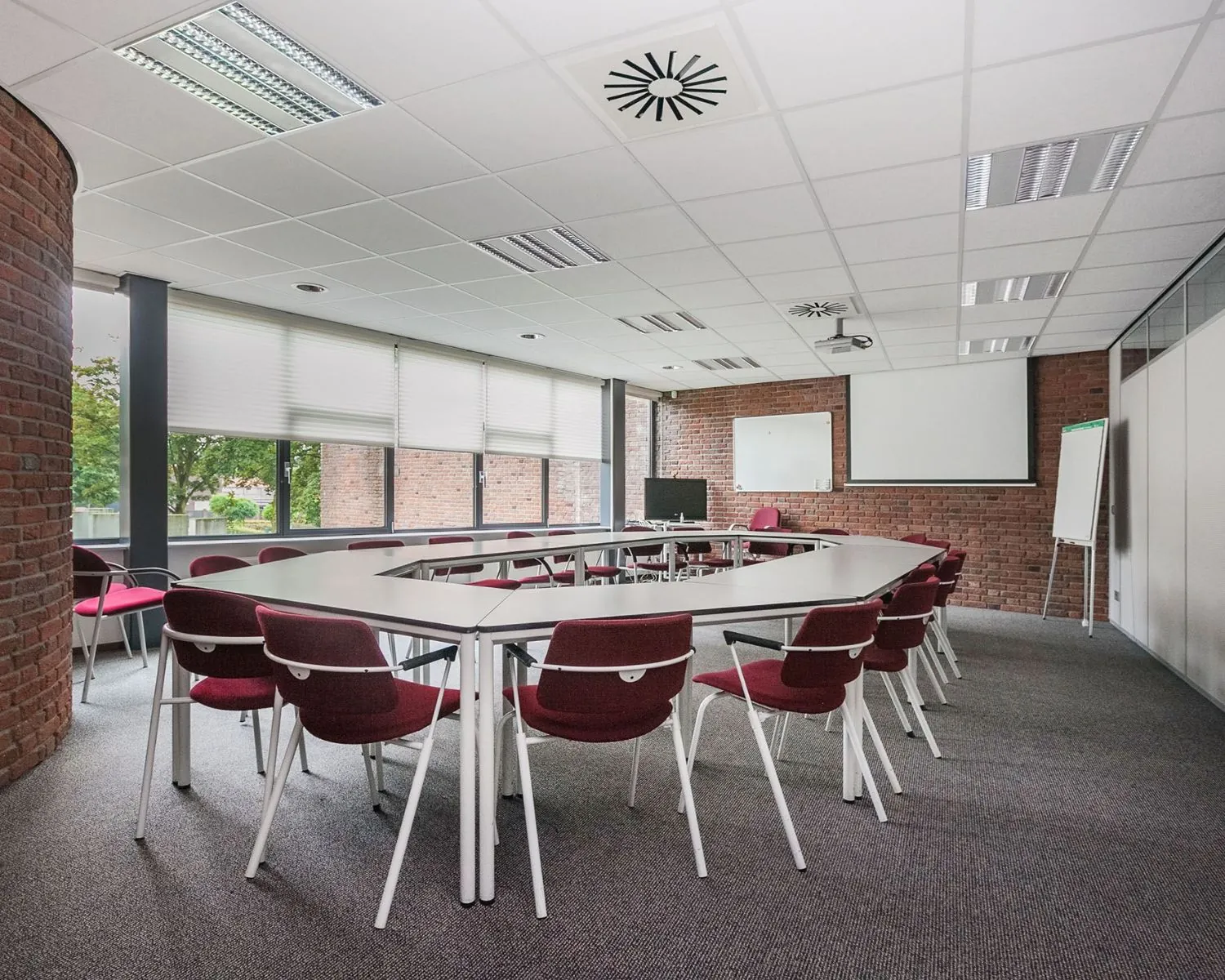 Vergaderruimte met U-vormige opstelling, rode stoelen en grote ramen in kantoorpand aan Kennedyplein 18.