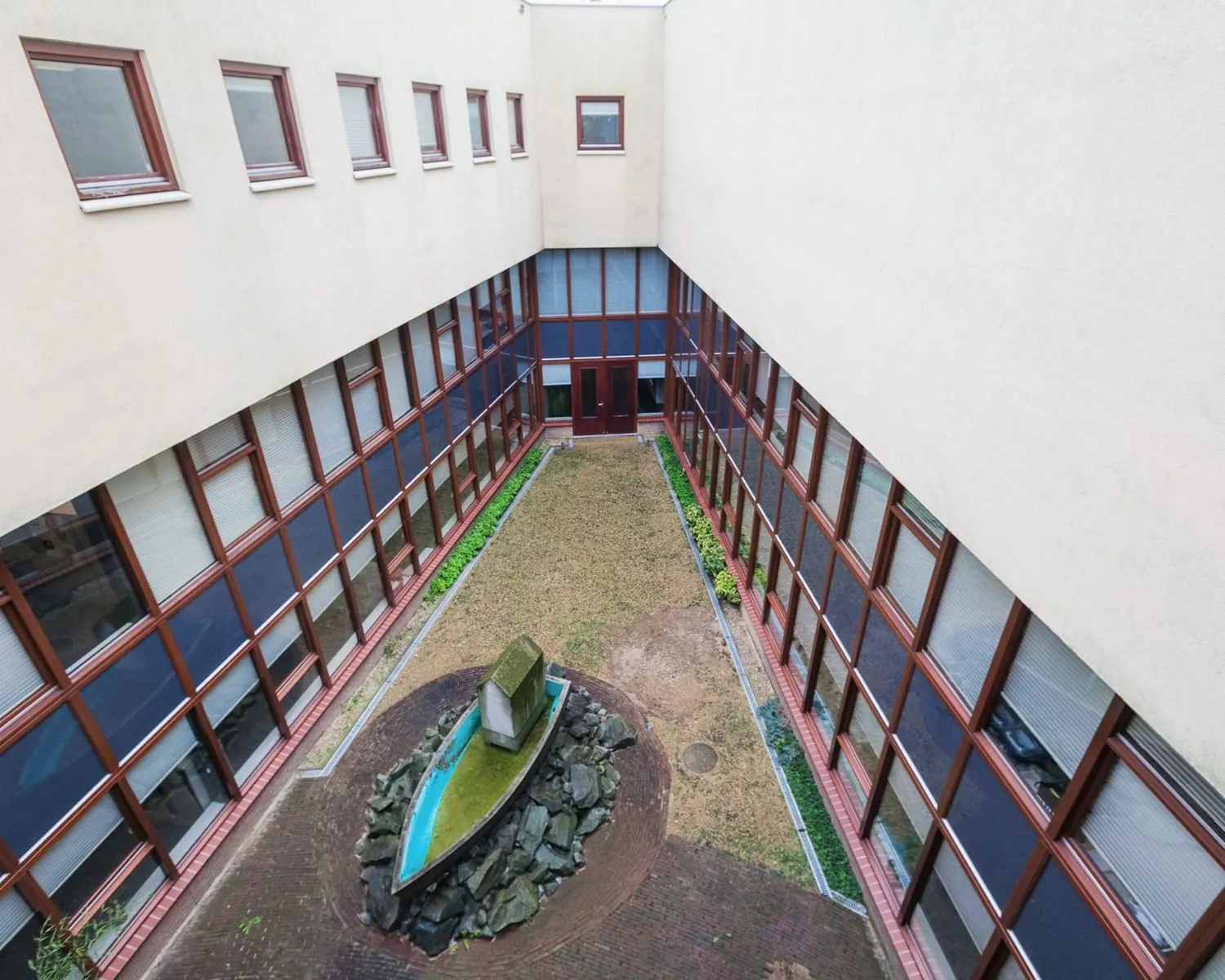 Binnentuin van kantoorruimte aan het Kennedyplein 18 met grasveld, planten en een kunstobject in de vorm van een boot.