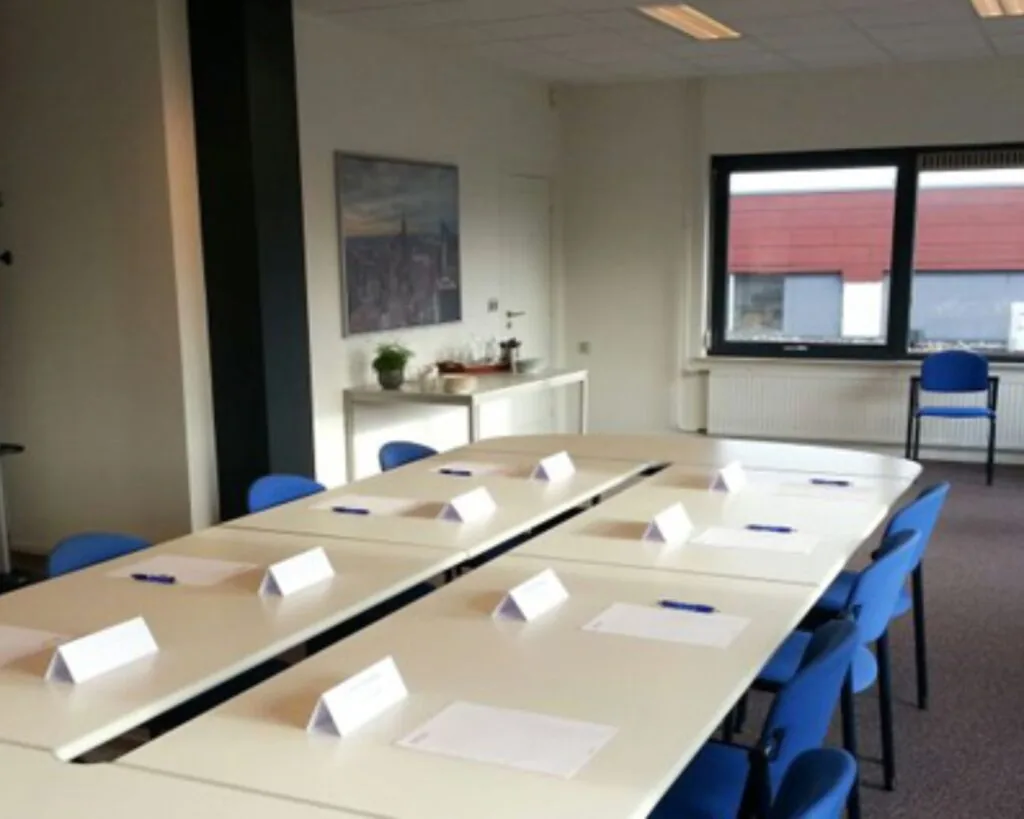 Vergaderruimte met opgestelde tafels en blauwe stoelen in het kantoorpand aan de Nusterweg 63.