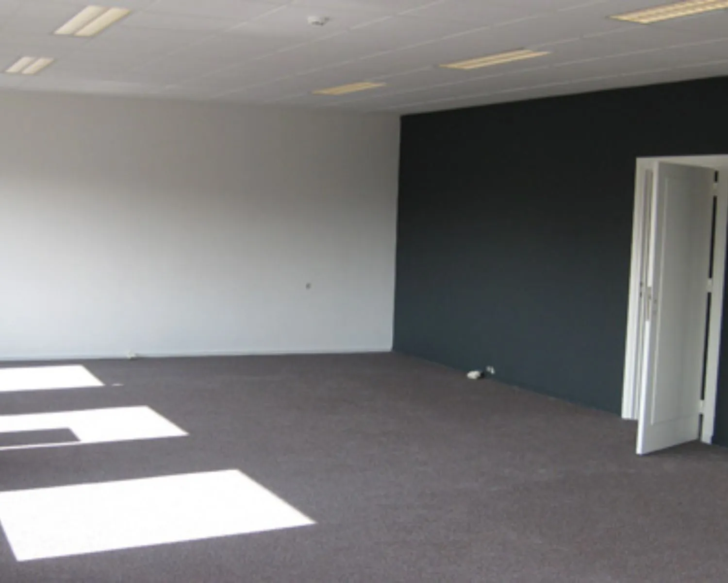 Lege kantoorruimte met grijze muren en donker tapijt aan de Nusterweg 63.