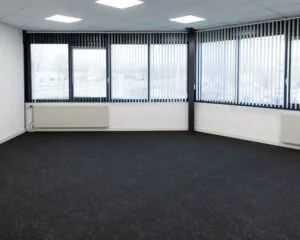 Lichte, lege kantoorruimte te huur aan de Parlevinkerweg 1-3 met grote ramen en donker tapijt.