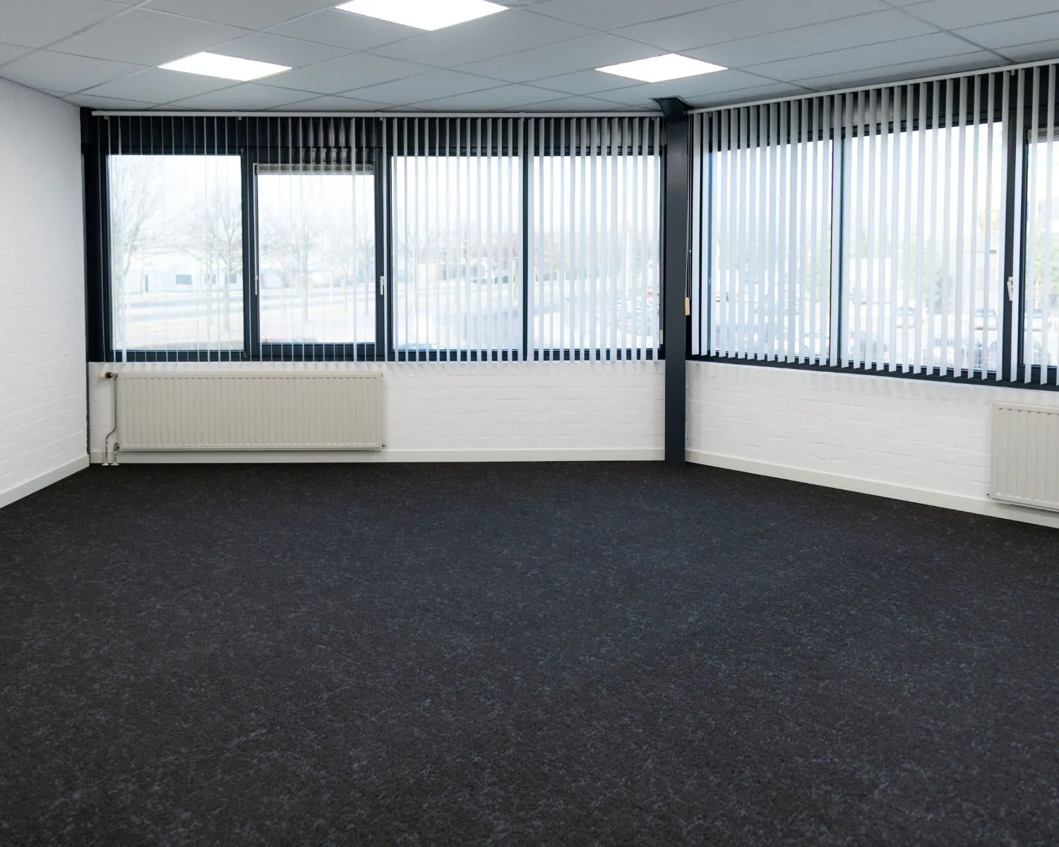Lichte, lege kantoorruimte te huur aan de Parlevinkerweg 1-3 met grote ramen en donker tapijt.