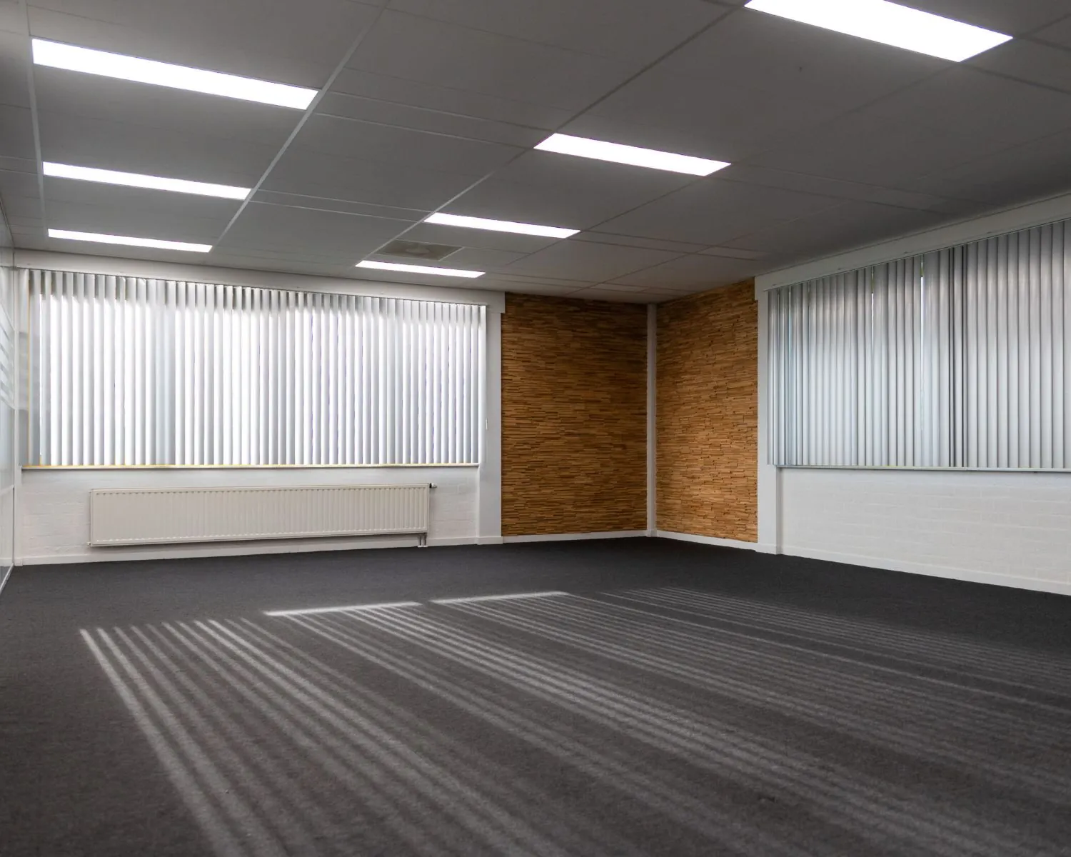 Lege kantoorruimte te huur aan de Parlevinkerweg 1 met tapijtvloer, systeemplafond en grote ramen met verticale lamellen.