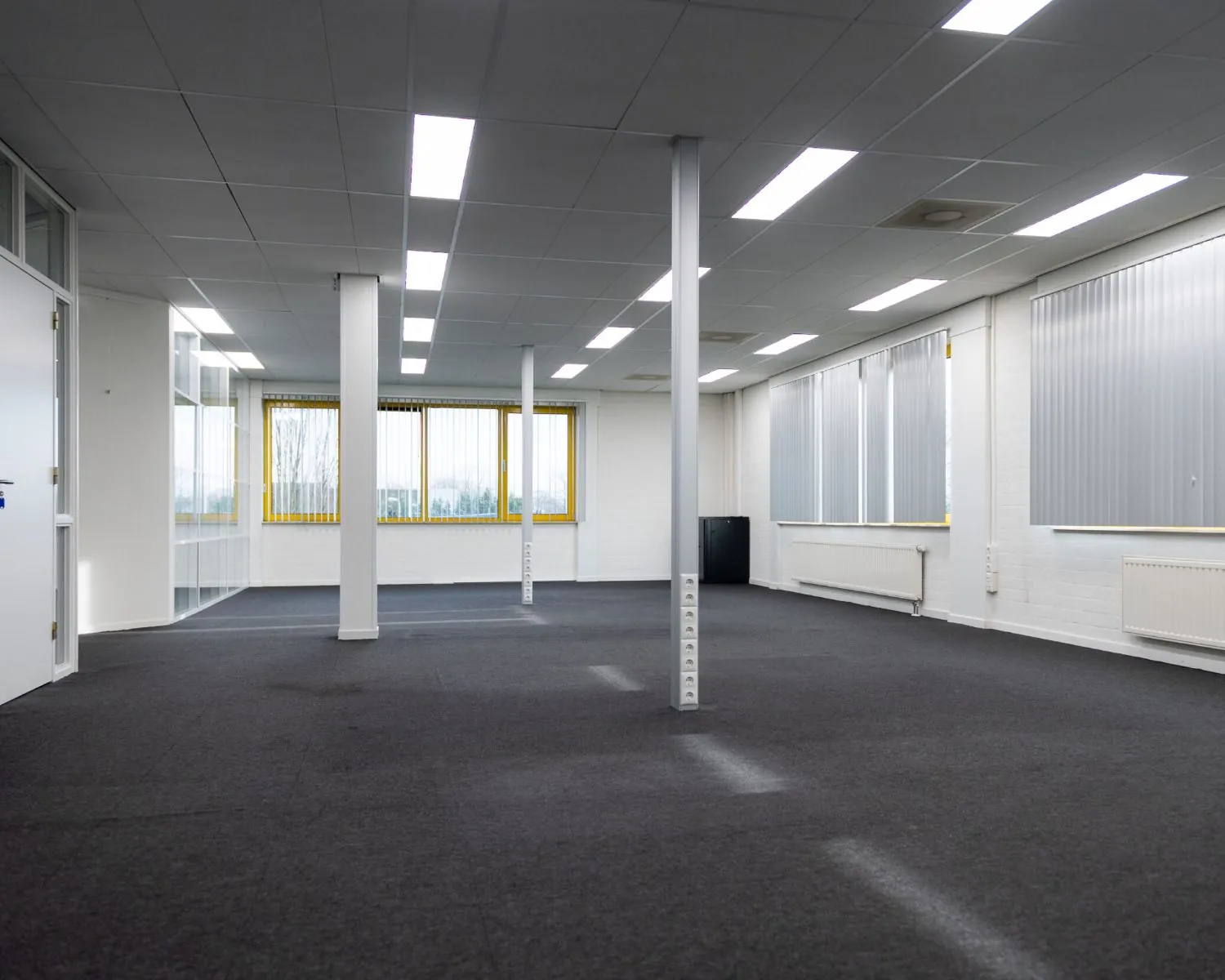 Lege kantoorruimte met grijze vloerbedekking en grote ramen aan de Parlevinkerweg 1-7.