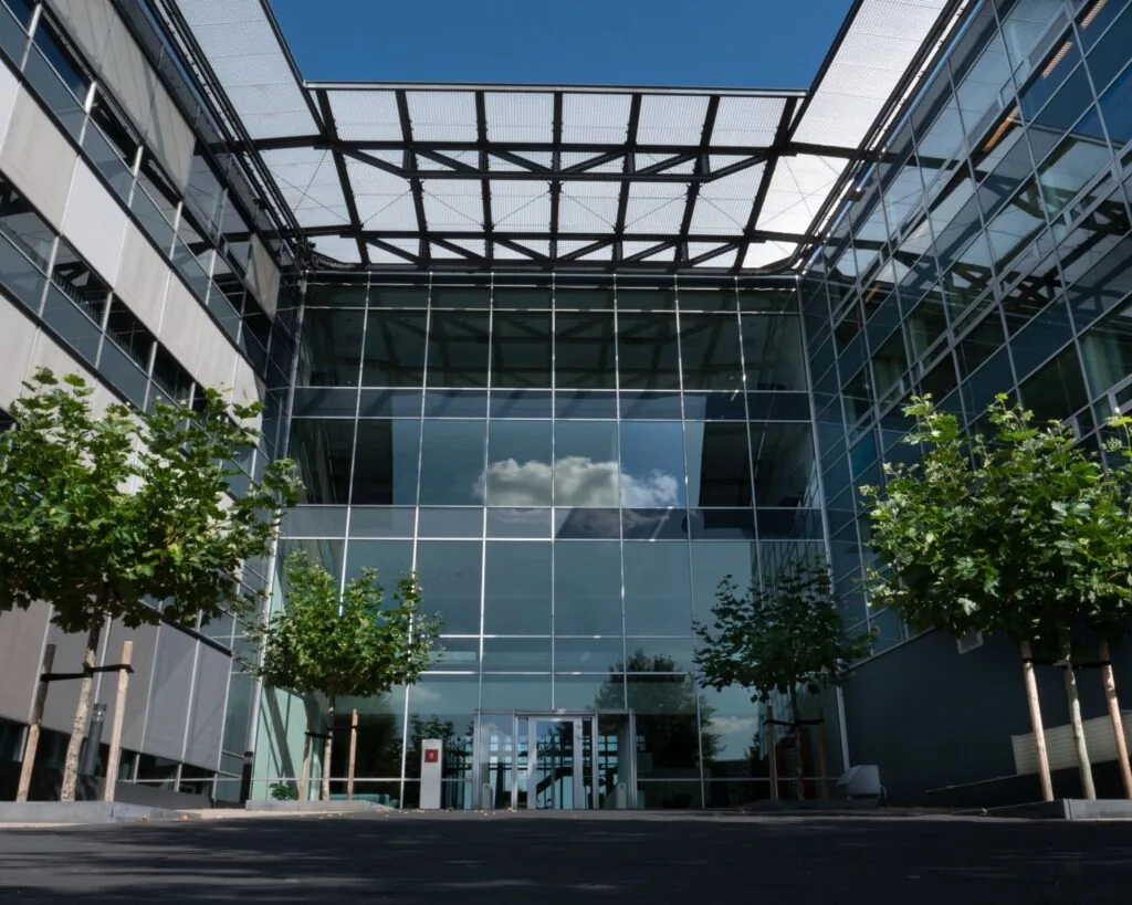 Moderne glazen entree van kantoorgebouw Snellius met jonge bomen aan weerszijden.