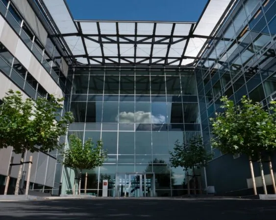 Moderne glazen entree van kantoorgebouw Snellius met jonge bomen aan weerszijden.