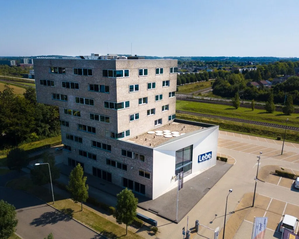 Kantoorgebouw met bedrijfsnaam "Lebe" aan de Transportlaan 30, omgeven door parkeerplaatsen en groen.