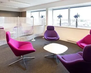 Moderne kantoorruimte aan de Transportlaan 30 met paarse designstoelen, een witte salontafel en grote ramen met uitzicht.