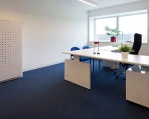 Moderne, lichte kantoorruimte met wit bureau, blauwe stoelen en grote ramen aan de Transportlaan 30.