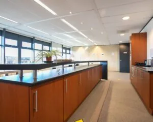 Moderne kantoorkeuken met houten kasten, zwarte werkbladen en grote ramen aan de Venrayseweg 180.