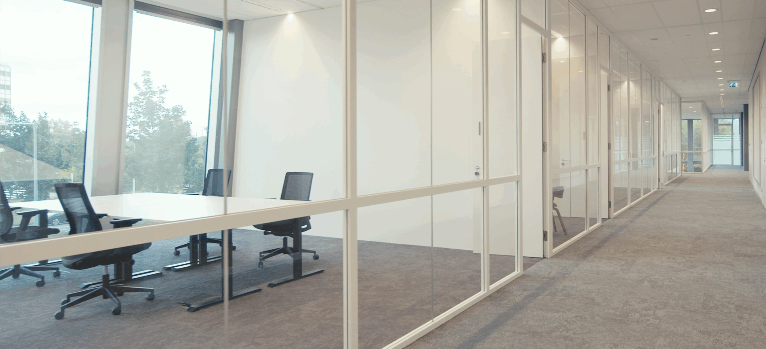 Moderne kantoorruimte met glazen wanden langs een brede, lichte gang.