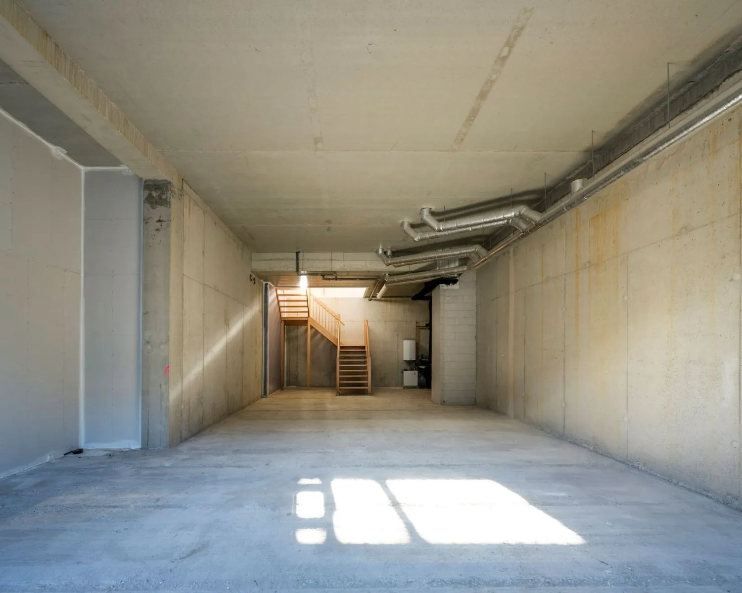Leeg kantoorpand met betonnen vloer en muren aan de Oostenburgermiddenstraat 123 in Amsterdam, met een houten trap naar een bovenverdieping.