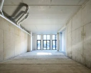 Leeg casco kantoorpand te huur aan de Oostenburgermiddenstraat 123-4 in Amsterdam met betonnen muren, plafond en grote ramen aan de voorzijde.