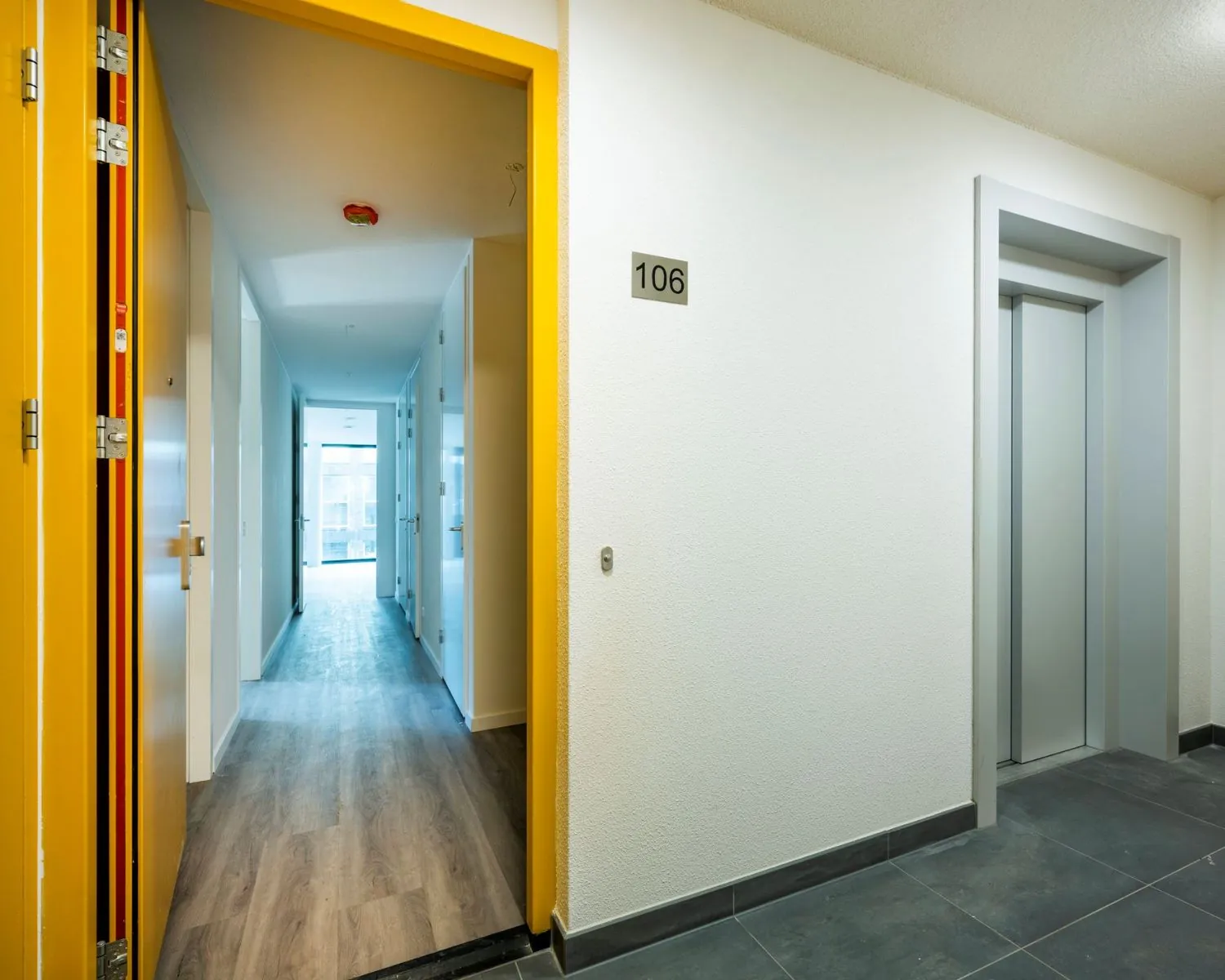 Entree van kantoorpand aan de Oostenburgermiddenstraat 123 in Amsterdam met open deur naar gang en zicht op lift en kamernummer 106.