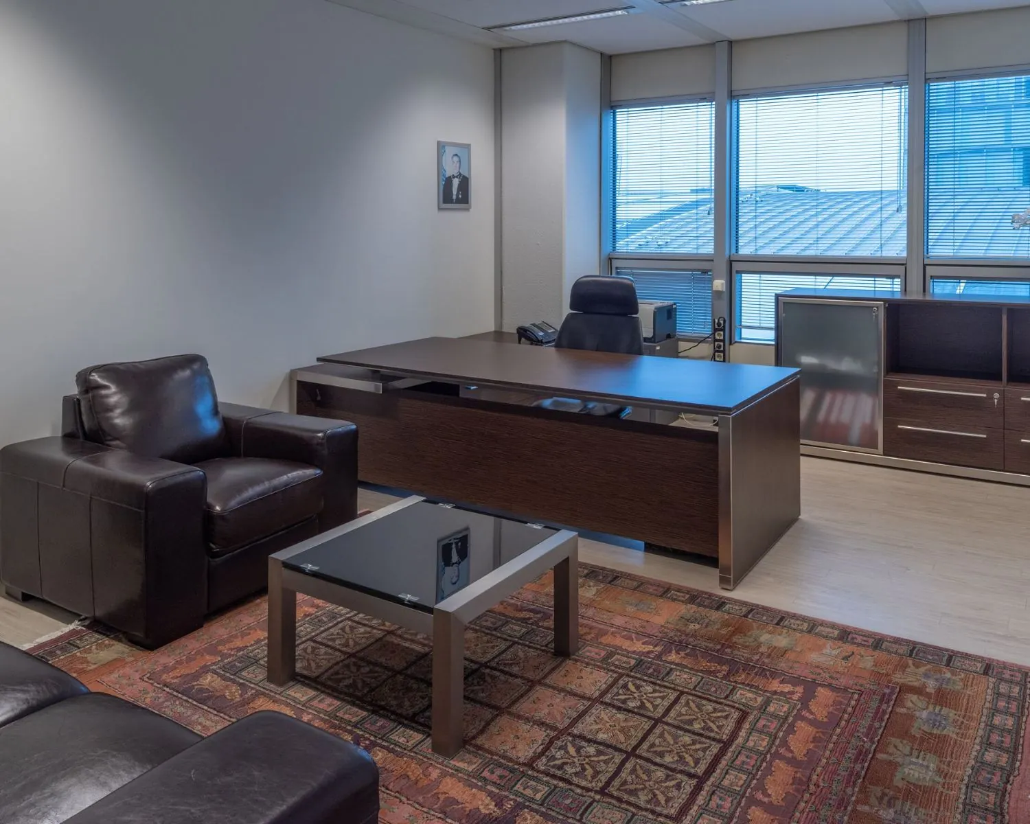 Moderne kantoorruimte aan de Strawinskylaan in Amsterdam Zuidas met leren stoelen, houten bureau en groot raam met jaloezieën.
