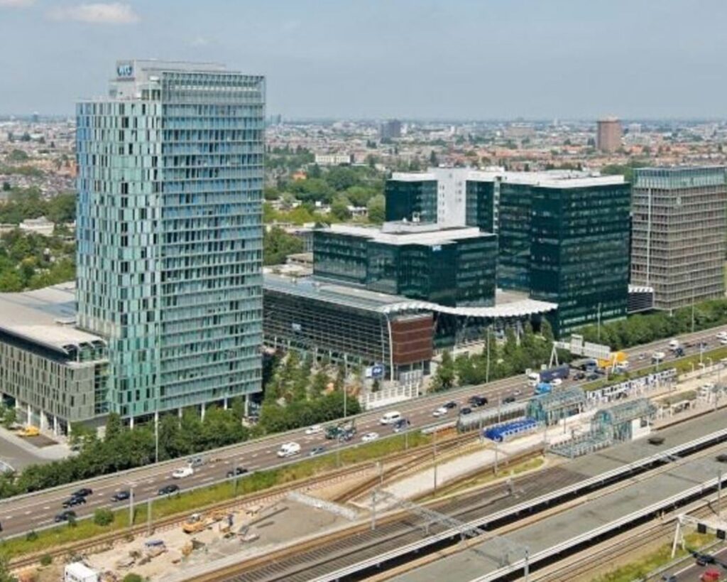 Luchtfoto van moderne kantoorgebouwen aan de Strawinskylaan op de Zuidas in Amsterdam, met snelweg en spoorlijn op de voorgrond.