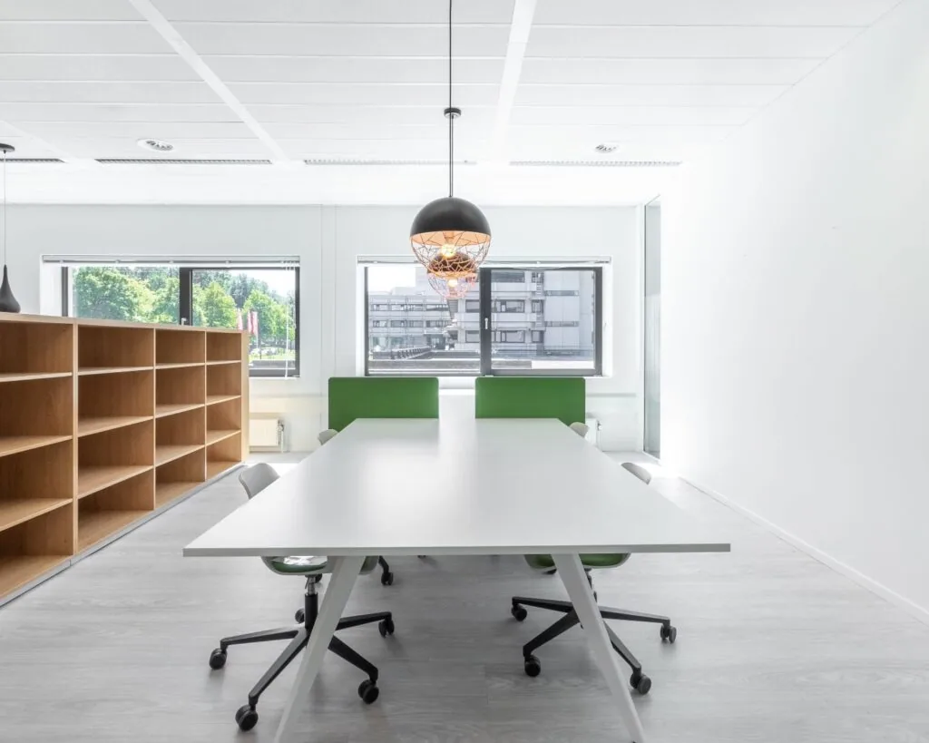 Moderne en lichte kantoorruimte aan de Bavincklaan 7 in Amstelveen met een grote werktafel, groene bureaustoelen en open wandkasten.