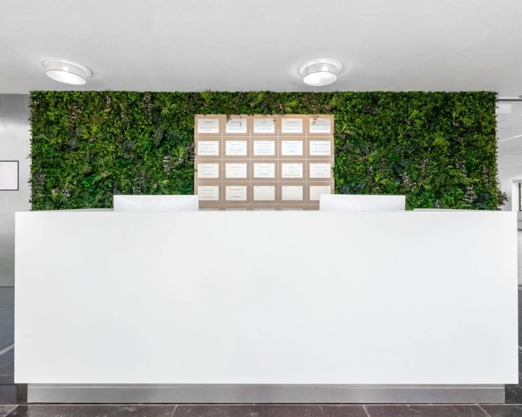 Witte balie in een moderne kantoorruimte aan de Bavincklaan 7 in Amstelveen, met een groene moswand en bedrijfsnaambord op de achtergrond.