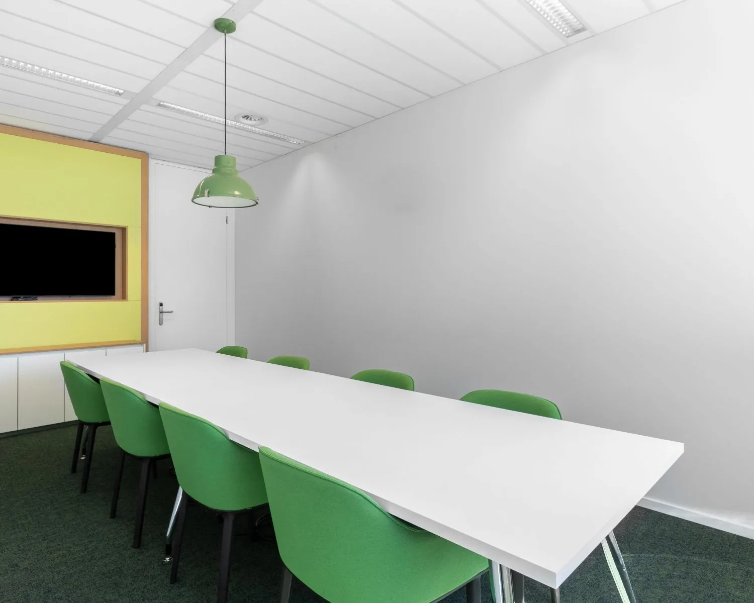 Vergaderruimte in Alstelveen met een witte tafel, groene stoelen en een ingebouwd tv-scherm aan de muur.