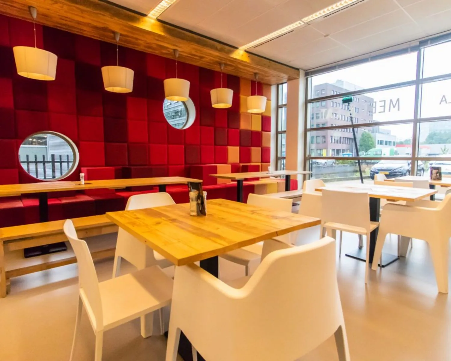 Moderne gemeenschappelijke kantoorruimte aan de Joop Geesinkweg 501 in Amsterdam met houten tafels, witte stoelen en een opvallende rode wandbekleding.