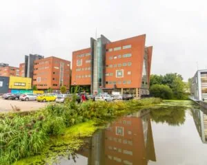 Modern kantoorgebouw aan de Joop Geesinkweg 501 in Amsterdam met parkeerplaats en vijver op de voorgrond.