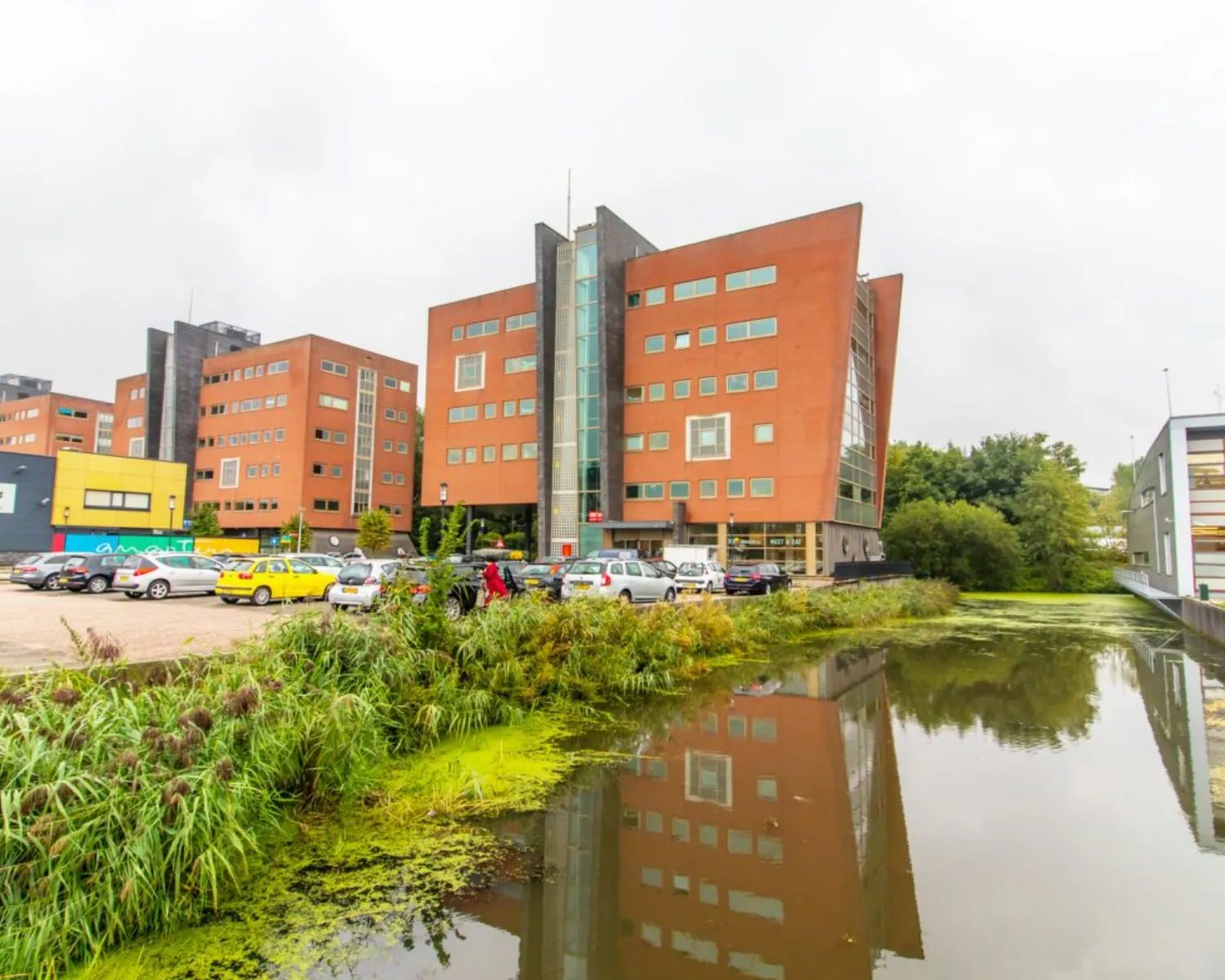 Modern kantoorgebouw aan de Joop Geesinkweg 501 in Amsterdam met parkeerplaats en vijver op de voorgrond.