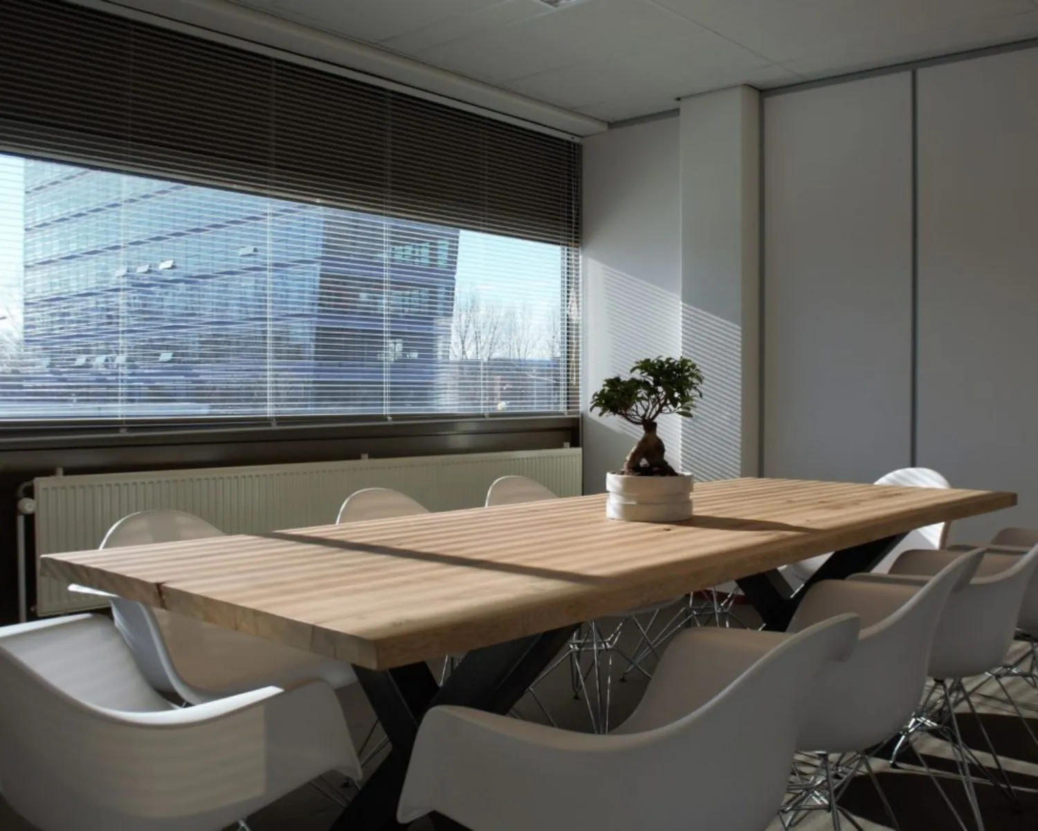 Vergaderruimte met een houten tafel, witte stoelen en uitzicht op kantoorgebouwen aan de Joop Geesinkweg 501 in Amsterdam.
