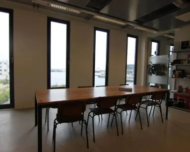 Vergaderruimte met grote houten tafel, zes stoelen en uitzicht op het water aan de Koivistokade 54 in Amsterdam.