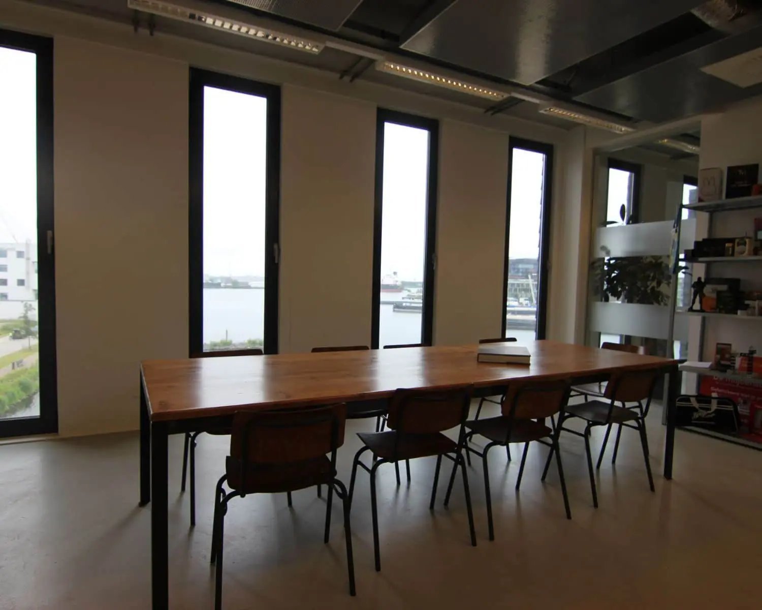 Vergaderruimte met grote houten tafel, zes stoelen en uitzicht op het water aan de Koivistokade 54 in Amsterdam.
