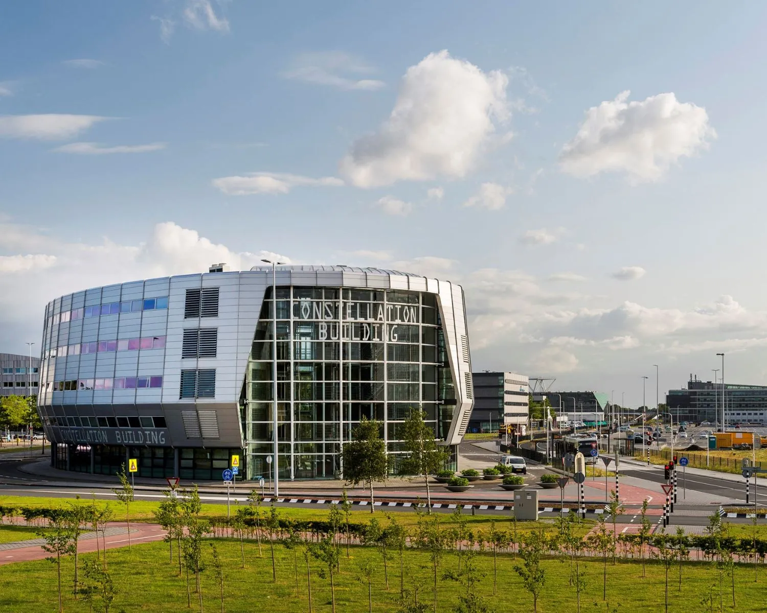 Modern kantoorgebouw genaamd Constellation Building aan het Stationsplein 416 in Schiphol, omringd door wegen en groenstroken.