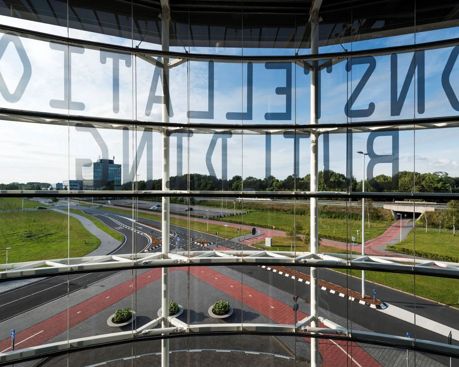 Uitzicht vanuit een modern kantoorgebouw aan het Stationsplein 416 in Schiphol op een weg met rotonde en groenstroken.