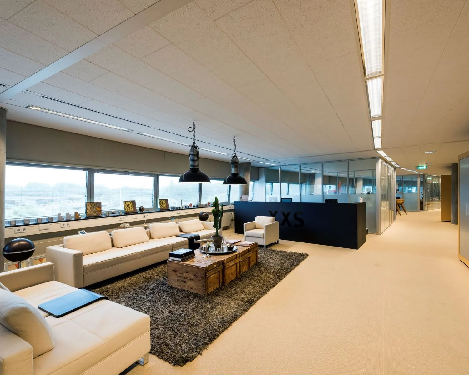 Moderne kantoorruimte met loungehoek, glazen vergaderruimtes en het logo van XXS op een zwarte balie aan het Stationsplein 416 in Schiphol.