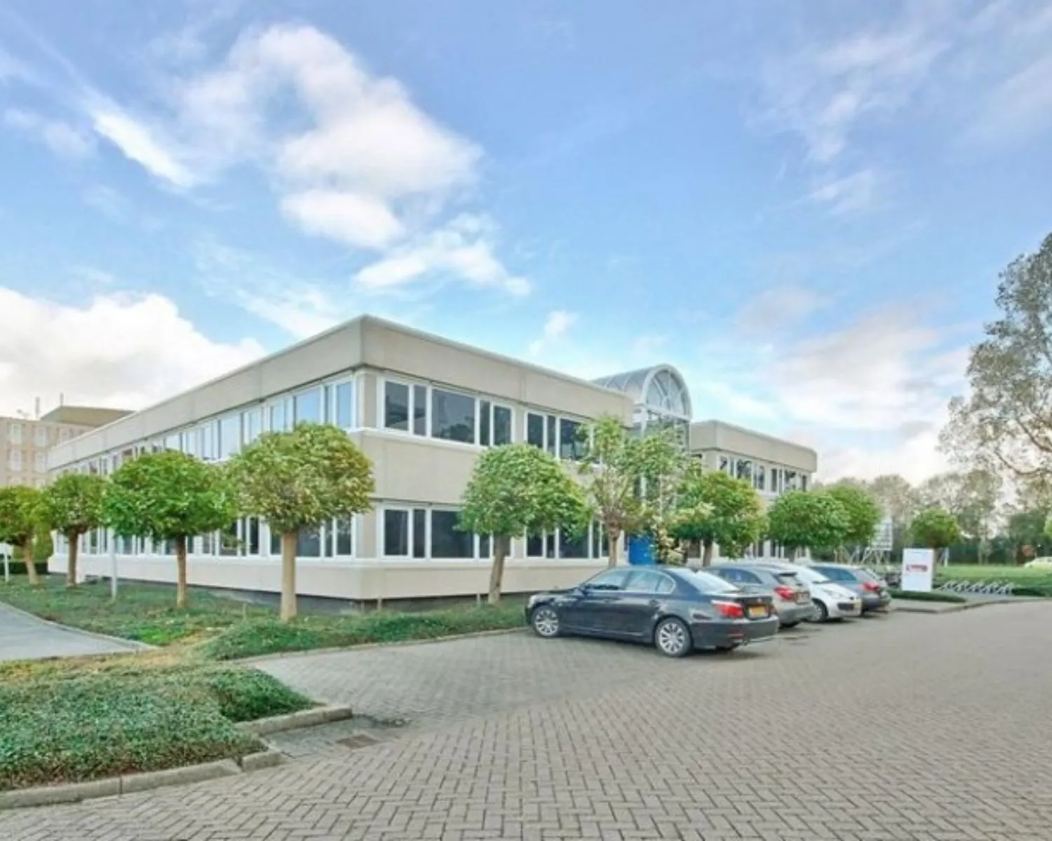 Twee verdiepingen tellend kantoorpand aan de Curieweg 7 in Spijkenisse met omliggende parkeerplaatsen en bomen.