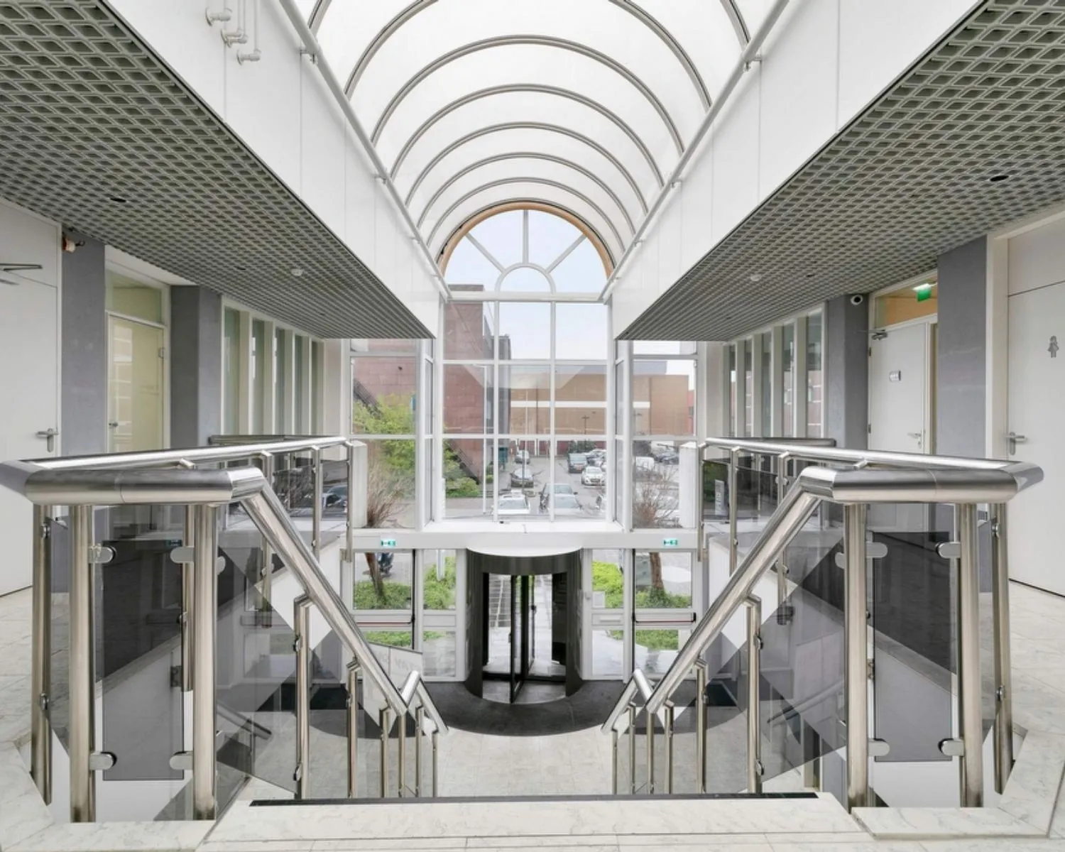 Moderne entreehal met glazen overkapping en dubbele trap in kantoorgebouw aan de Curieweg 7 in Spijkenisse.