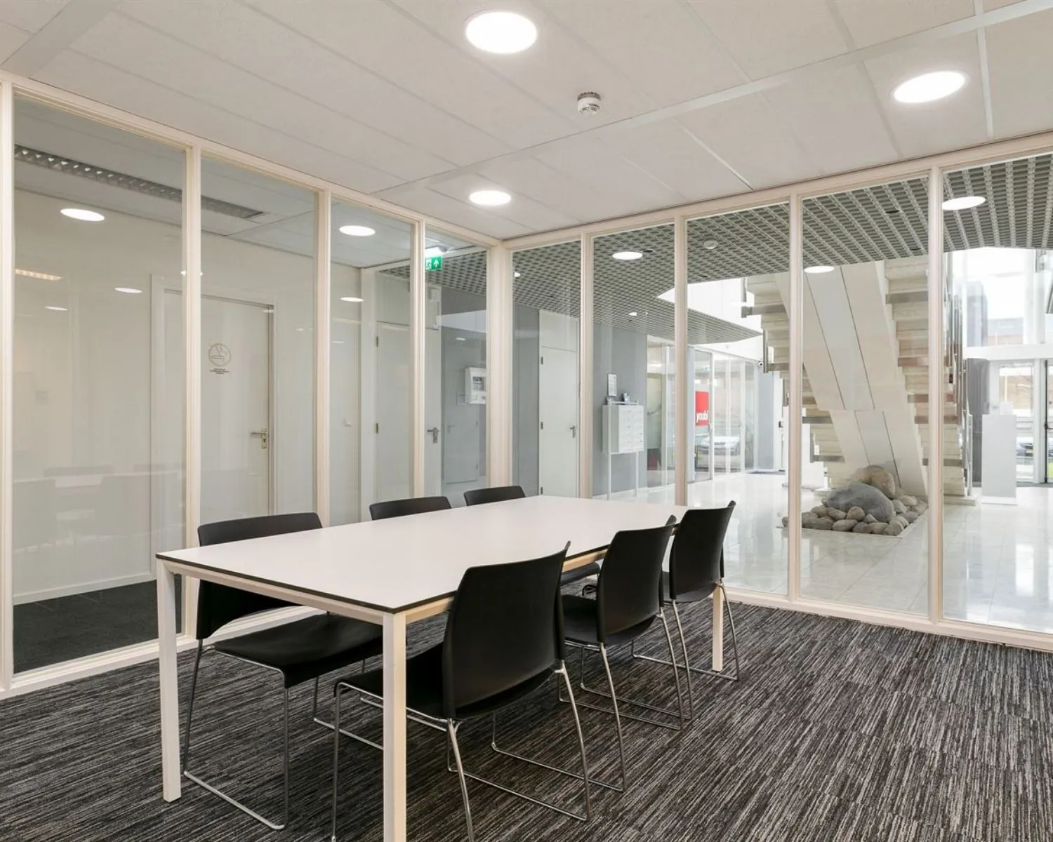 Vergaderruimte met glazen wanden en zes zwarte stoelen aan een witte tafel in een kantoor aan de Curieweg 7 in Spijkenisse.