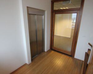 Entree van een kantoorruimte aan de De Ruijterkade 142 in Amsterdam met een houten vloer, glazen deur en liftdeur.