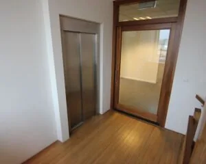 Entree van een kantoorruimte aan de De Ruijterkade 142 in Amsterdam met een houten vloer, glazen deur en liftdeur.