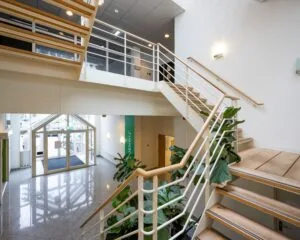 Moderne entreehal met houten trap, veel daglicht en planten in een kantoorpand aan de Gyroscoopweg 144 in Amsterdam.