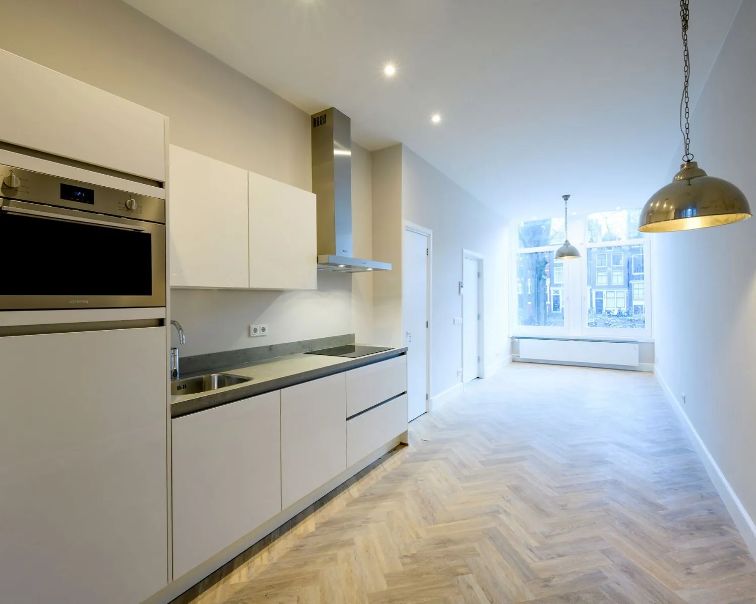 Moderne kantoorruimte aan de Herengracht 352 in Amsterdam met een open keuken, houten visgraatvloer en grote ramen met uitzicht op de gracht.