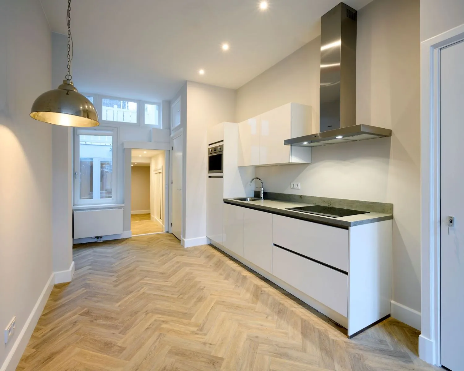 Moderne kitchenette in een strakke kantoorruimte aan de Herengracht 352 in Amsterdam, met visgraatvloer en ingebouwde apparatuur.
