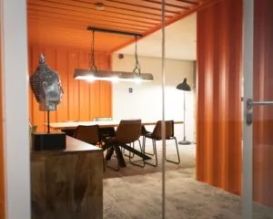 Vergaderruimte met oranje wanden, moderne verlichting en een houten tafel met bruine stoelen aan de Hofmanweg in Haarlem.