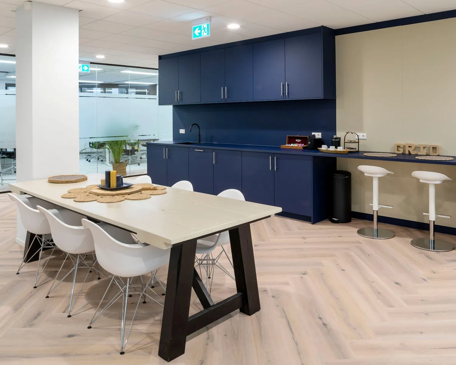 Moderne kantoorkeuken met blauwe kasten, een lange houten tafel en witte stoelen aan de Kabelweg 57 in Amsterdam.