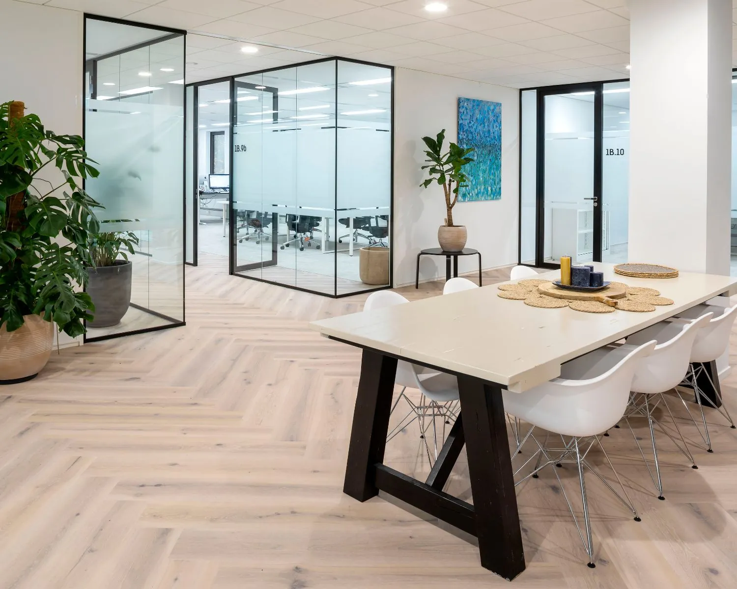Moderne kantoorruimte aan de Kabelweg 57 in Amsterdam met glazen vergaderruimtes, houten visgraatvloer en een lange vergadertafel met witte stoelen.