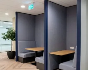 Moderne blauwe zithoeken met houten tafels in een kantoorruimte aan de Kabelweg 57 in Amsterdam.