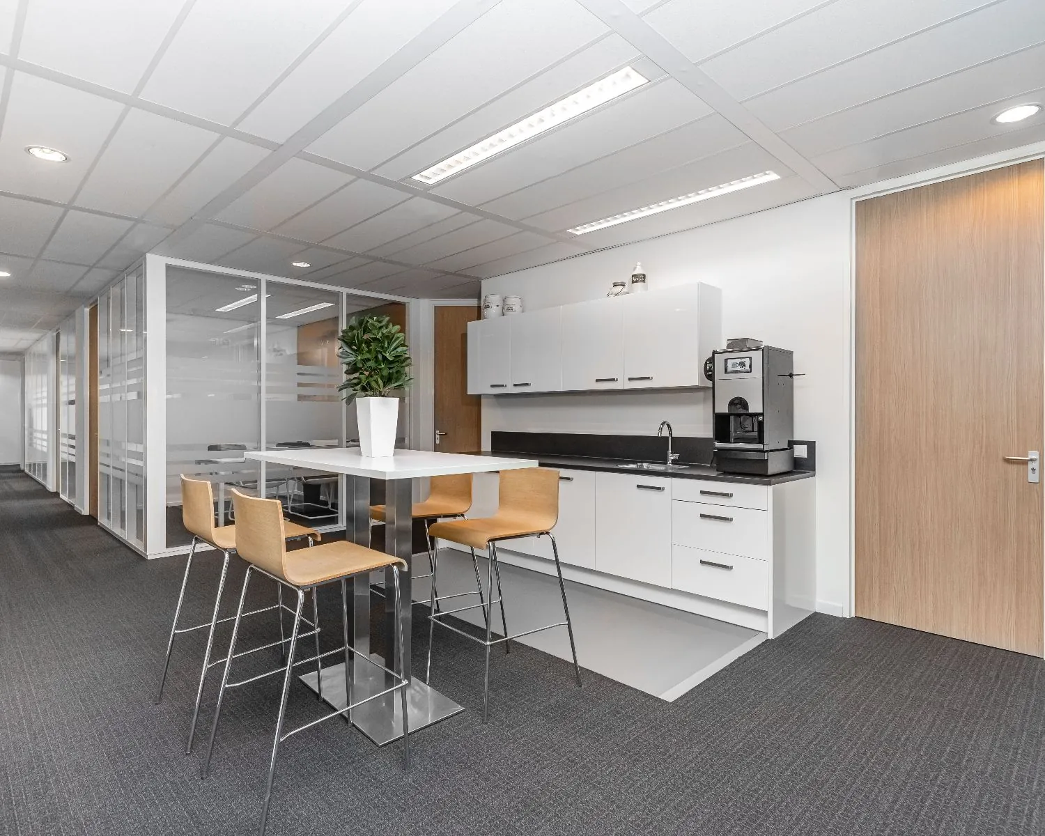 Moderne pantry met hoge tafel, barkrukken en koffiemachine in een kantoorruimte aan de Louis Braillelaan 80 in Zoetermeer.