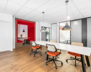 Moderne kantoorruimte aan de Meester B.M. Teldersstraat in Arnhem met een lange vergadertafel, kleurrijke bureaustoelen en een rode zithoek.