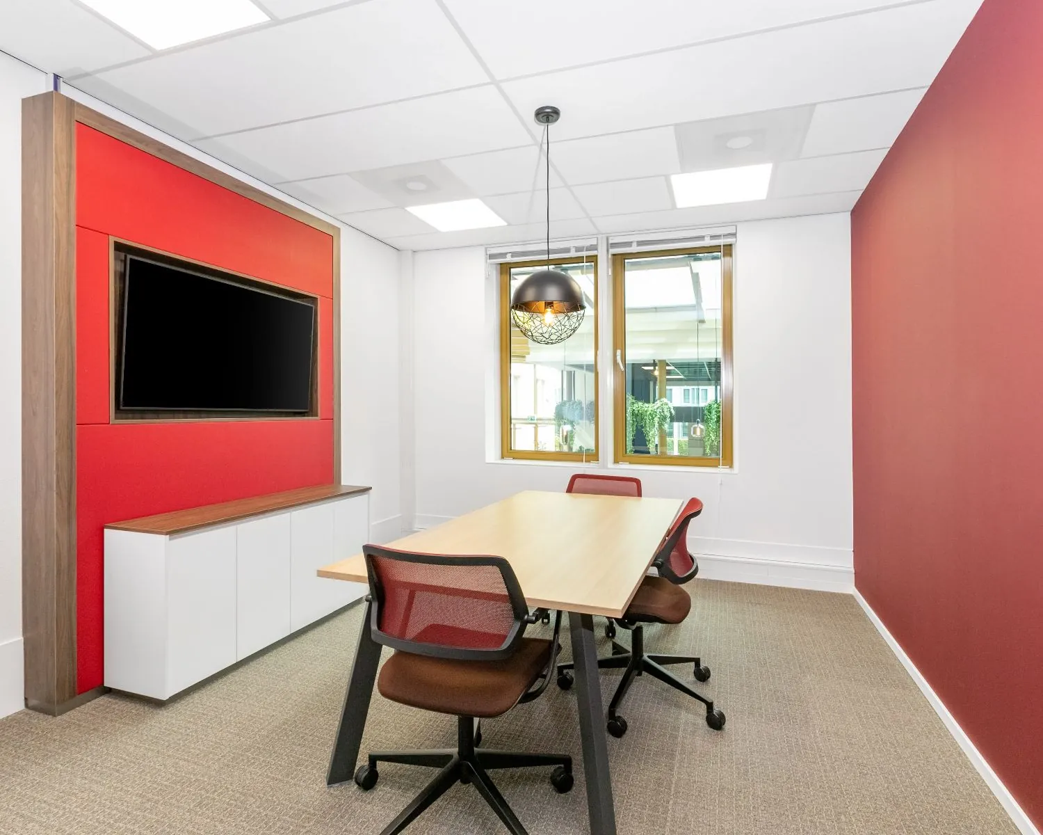 Moderne vergaderruimte in kantoor aan de Meester B.M. Teldersstraat 7 in Arnhem met rode accentmuur, houten tafel en flatscreen.