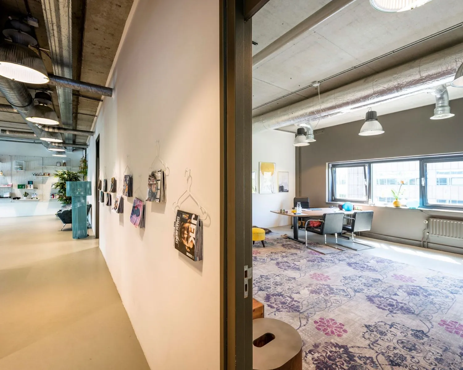 Moderne kantoorruimte aan de Overschiestraat 180 in Amsterdam met vergadertafel, kleurrijk vloerkleed en industriële plafonddetails.