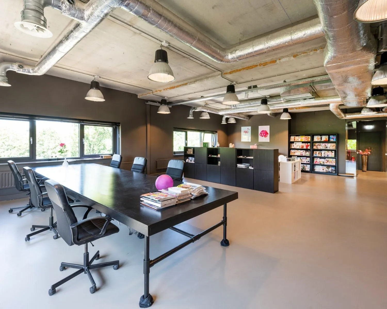 Moderne kantoorruimte aan de Overschiestraat 180 in Amsterdam met industriële inrichting, vergadertafel en tijdschriftenrek.