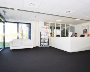 Moderne ontvangstruimte met een witte balie, een bank en grote ramen in een kantoor aan de Platinaweg 25 in Den Haag.